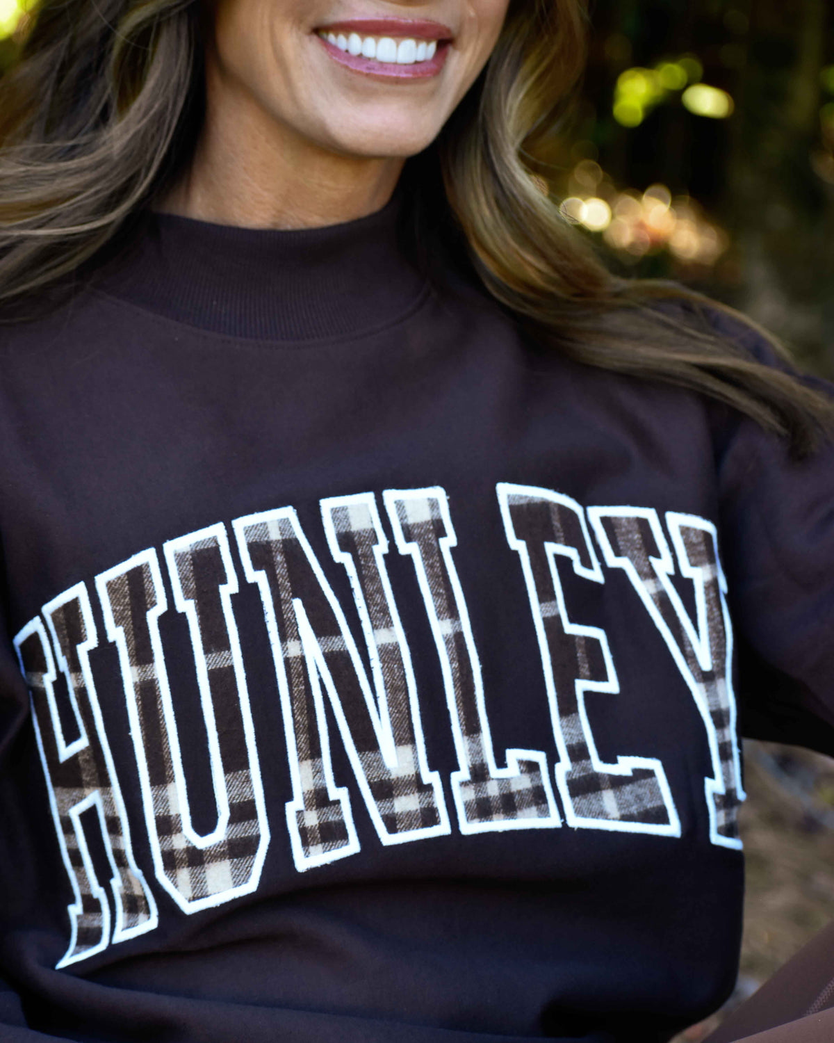 Close-up of plaid HUNLEY lettering with white outlines on the brown Fall Flannel sweatshirt.