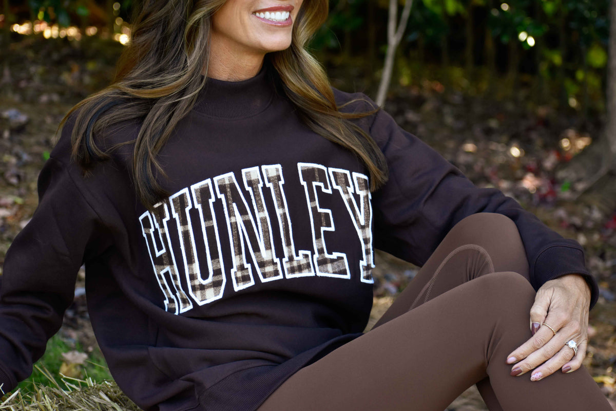 Brown HUNLEY Fall Flannel mock-neck sweatshirt with plaid lettering, styled with brown leggings.